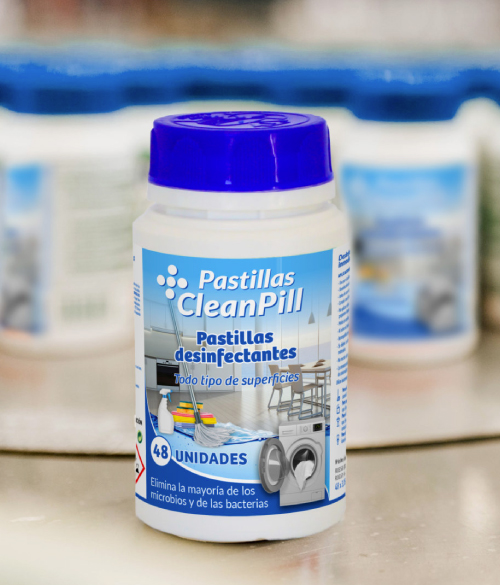 Envase de pastillas desinfectantes de la marca CleanPill, con tapa azul y etiqueta azul clara. En la etiqueta se lee: 'Pastillas CleanPill - Pastillas desinfectantes - Todo tipo de superficies - 48 unidades'. También se observan imágenes ilustrativas de una lavadora, sillas y una piscina inflable, indicando su uso versátil. En la parte inferior, un texto señala que elimina la mayoría de los microbios y las bacterias.